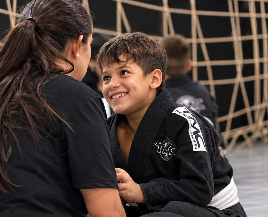 Criança sorrindo durante aula de Jiu-Jitsu Kids, conversando com a professora
