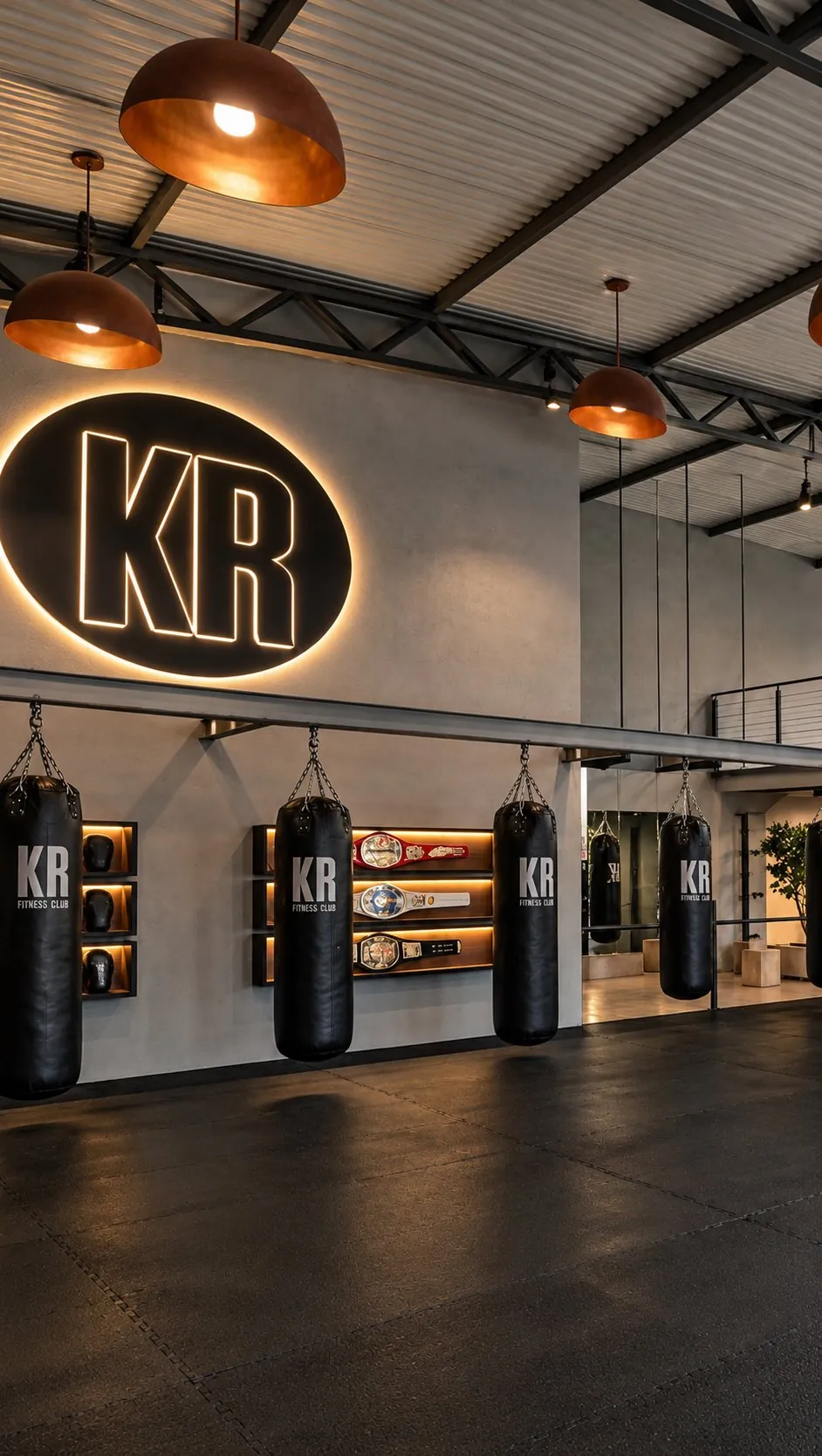 Área de lutas da KR com sacos de pancada, cinturões expostos e o logo KR iluminado na parede